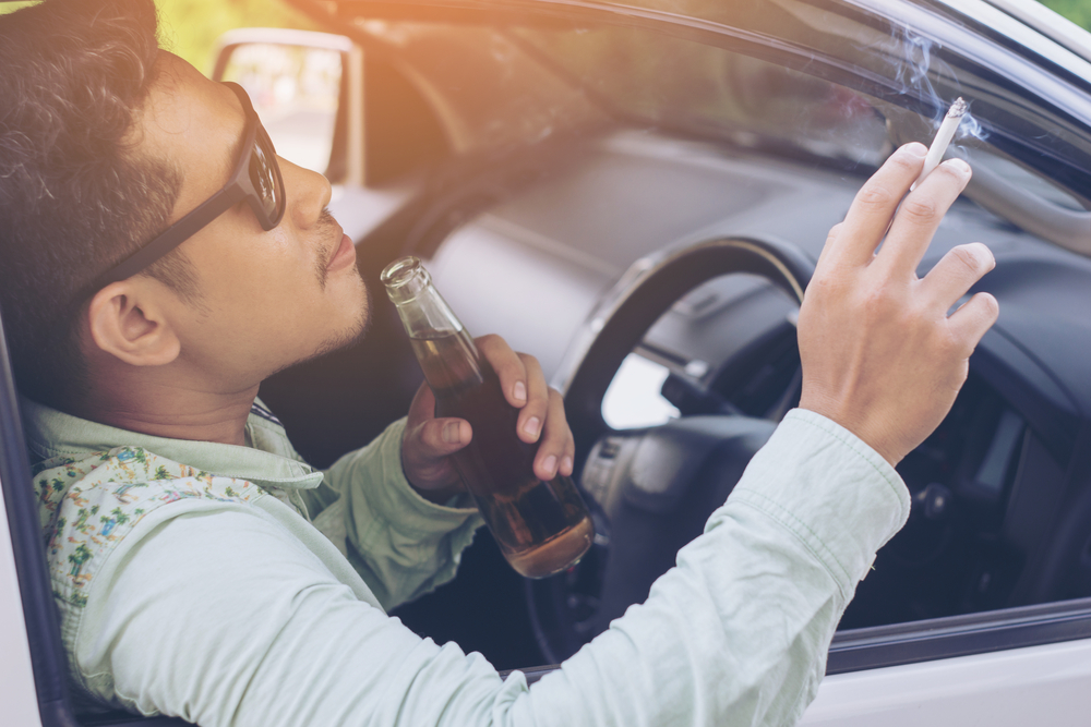 a young man lit a cigarette driving the car and drinking beer selective focus