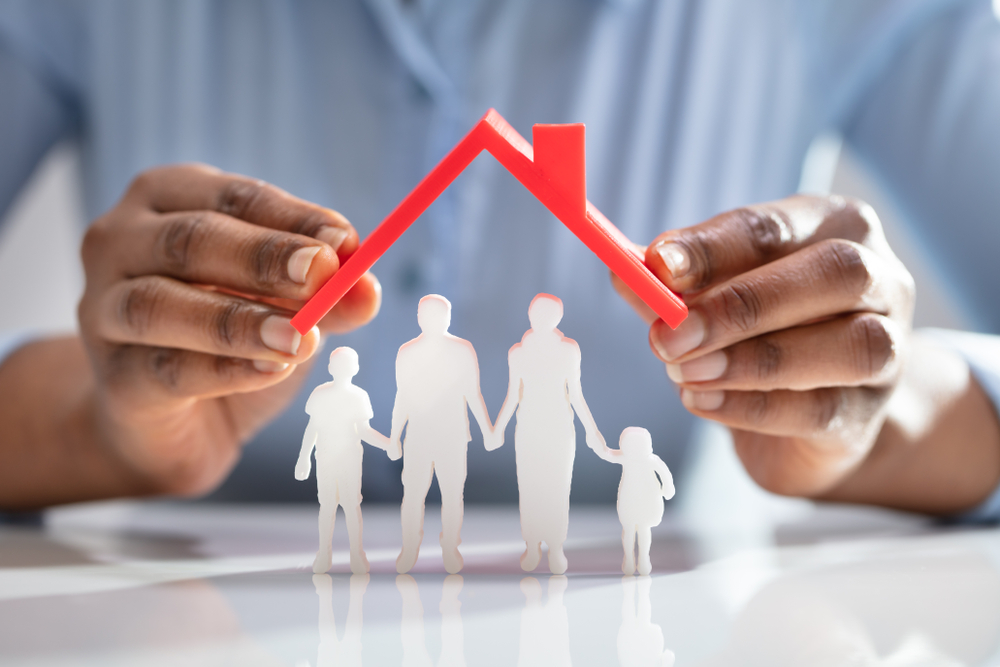A Person's Hand Protecting Family Figures With Red Roof