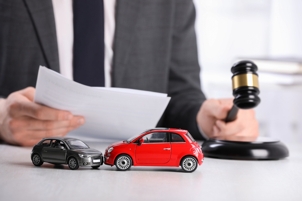 Auto accident law. Man with document and gavel at table indoors, focus on toy cars