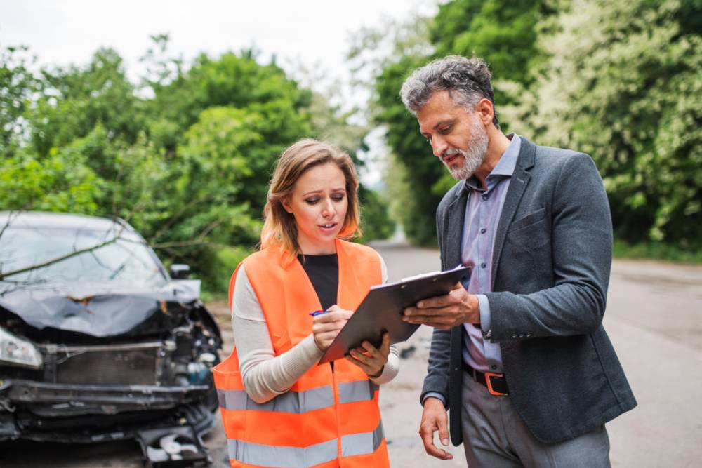 An insurance agent talking to a woman outside on the road after a car accident.