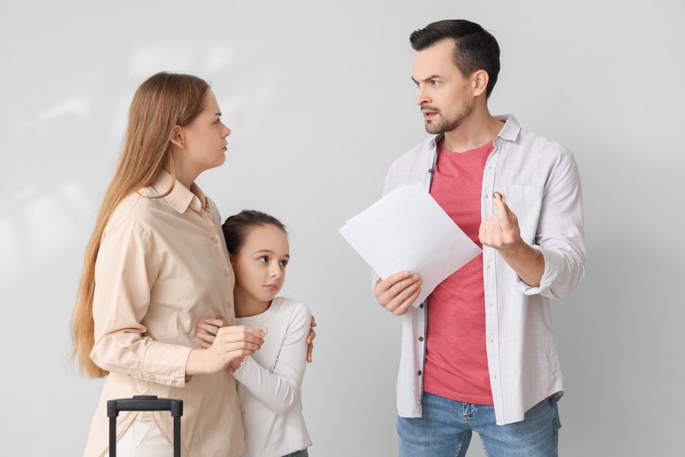 Sad little girl and her parents getting divorce on light background