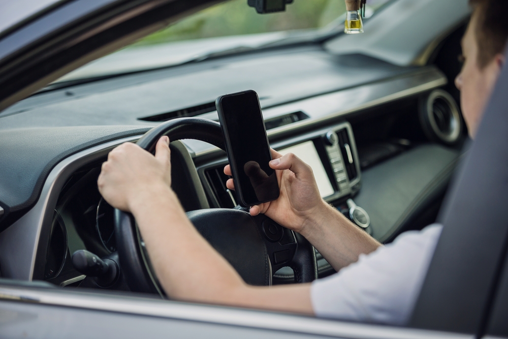 Casual driver guy distracted by his phone while in front of the steering wheel, using his smartphone with one hand while driving