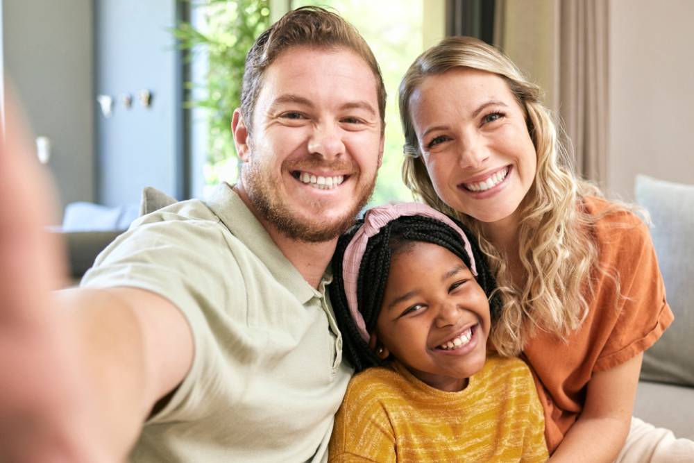 Happy family, adoption and smile for selfie love, relax or bonding in happiness together at home